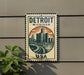 A metal sign with the text "DETROIT MICHIGAN USA" and an illustration of a city skyline, mounted on a wall.