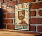 A vintage Jersey postage stamp is displayed on a brick wall, featuring a shield with a lion and a castle.