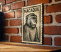 A framed illustration of a monkey is displayed on a brick wall.