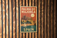 A vintage-style metal sign with the text "PALMA DE MAJORCA" and "SPAIN" printed on it, hanging on a wooden wall.