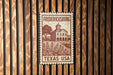 A metal sign with a wooden border displaying the text "FREDERICKSBURG TEXAS - USA" and an illustration of a building surrounded by trees.