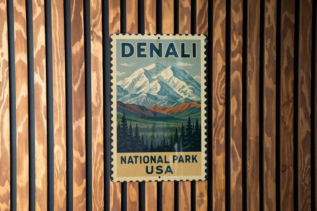 A vintage-style metal sign with the text "DENALI NATIONAL PARK USA" displayed on a wooden wall.