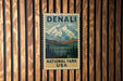 A vintage-style metal sign with the text "DENALI NATIONAL PARK USA" displayed on a wooden wall.