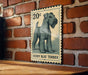 A vintage-style 20c postage stamp featuring a blue terrier dog is displayed on a brick wall.