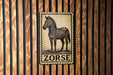 A metal sign with a zebra illustration is mounted on a wooden wall.