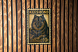 A metal stamp featuring a dog, with the text "Keeshond" and "10c" printed on it, is displayed on a wooden wall.