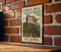 A vintage postage stamp featuring the Sigiriya Rock, a famous landmark in Sri Lanka, is displayed on a brick wall.