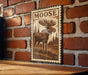 A wooden table with a framed image of a moose on it, mounted on a brick wall.