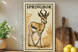 A framed illustration of a gazelle or antelope, with the text "SPRINGBOK" on the top, is displayed on a shelf next to a wooden cutting board and a potted plant.