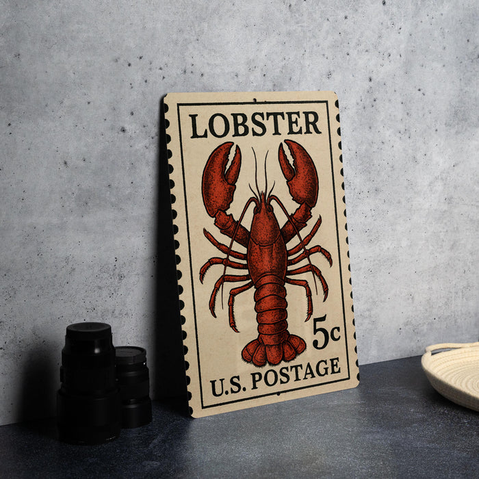 A U.S. postage stamp featuring a lobster illustration, placed on a table next to some black camera lenses.