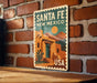 A vintage-style metal sign with the text "SANTA FE NEW MEXICO USA" displayed on a brick wall.