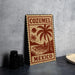 A wooden sign with a tropical palm tree design and the text "COZUMEL MEXICO" is displayed on a gray wall.