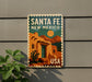 A vintage-style sign for Santa Fe New Mexico, featuring a desert landscape with a cactus and mountains in the background.