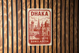 A sign displaying the name "Dhaka" and the word "BANGLADESH" in a stylized design, mounted on a wooden wall.