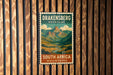 A vintage-style poster of the Drakensberg Mountains in South Africa, featuring a scenic mountain landscape with a winding river.