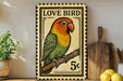 A vintage postage stamp featuring a colorful parrot perched on a branch, with the text "LOVE BIRD" and "5¢" printed on it. The stamp is displayed on a shelf next to a wooden cutting board and a potted plant.
