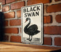 A sign featuring a black swan is mounted on a brick wall.