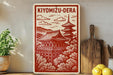 A red and white sign with an illustration of a traditional Japanese temple, surrounded by trees, is displayed on a shelf next to a wooden cutting board and some potted plants.