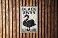 A sign with the text "BLACK SWAN" and an illustration of a black swan is displayed on a wooden wall.