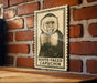 A framed illustration of a white-faced capuchin monkey is displayed on a brick wall.