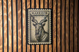 A metal stamp with a black and white illustration of a horned animal, likely a goat or ram, is mounted on a wooden wall.