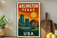 A vintage-style metal sign with the text "ARLINGTON TEXAS USA" displayed on it, featuring an illustration of a city skyline and a sun.