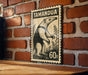A vintage-style stamp featuring a black and white illustration of a wild animal, likely a badger, mounted on a brick wall.