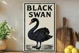 a sign with a black swan illustration, placed on a wooden surface next to a wooden cutting board and some lemons.