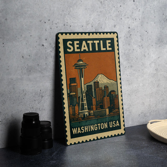 A metal stamp depicting the Seattle skyline with the Space Needle, placed on a gray surface next to some black camera lenses.