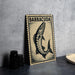 a framed print of a fish, specifically a Barracuda, with the word "Barracuda" written on it. The print is placed on a table next to some black camera lenses.