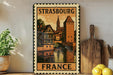 A vintage-style metal sign with a picture of a town and the text "STRASBOURG FRANCE" is displayed on a wall, accompanied by a wooden cutting board and a potted plant.