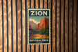 A vintage-style metal sign with the word "ZION" and "NATIONAL PARK U.S.A." printed on it, hanging on a wooden wall.