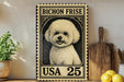A vintage-style metal stamp featuring a Bichon Frise dog, with the text "BICHON FRISE" and "USA 25" printed on it. The stamp is placed on a wooden surface, surrounded by various kitchen items such as a wooden cutting board, a lemon, and a potted plant.