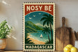 A vintage-style stamp depicting a tropical beach scene with palm trees, a sailboat, and mountains in the background, along with the text "NOSY BE MADGASCAR".