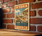 A vintage-style poster of a Greek island, featuring a coastal town with houses and boats, is displayed on a brick wall.