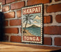 A vintage-style sign with the text "HA'APAI TONGA" and a palm tree illustration is displayed on a brick wall.