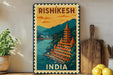 A vintage-style metal sign with a colorful illustration of a temple and a river, along with the text "RISHIKESH INDIA" on it, is displayed on a shelf next to a potted plant and a wooden cutting board.