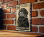A black and white postage stamp featuring a dog, likely a Labrador Retriever, is displayed on a brick wall.