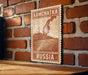 A wooden sign with a map of Kamchatka, Russia, mounted on a brick wall.