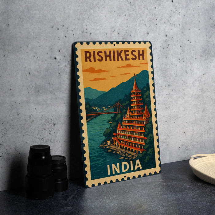 A vintage-style metal sign with a colorful illustration of a temple and a bridge, along with the text "RISHIKESH INDIA" on it, is displayed on a gray wall.
