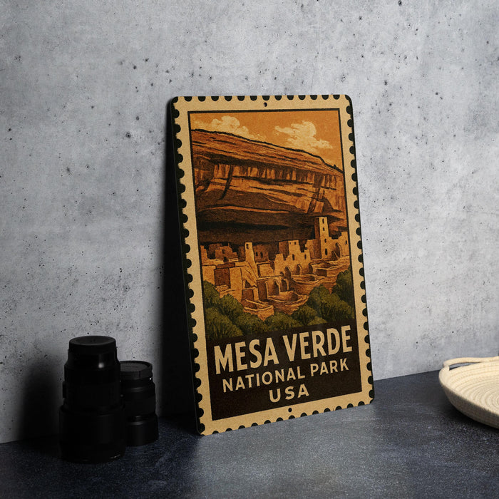 A metal sign with a vintage-style illustration of the mesa terraces in the National Park of Mexico, accompanied by text that reads "MESA VERDE NATIONAL PARK USA".