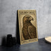 A framed image of a golden eagle, with the text "GOLDEN EAGLE" and "AQUILA CHRYSAEATOS" printed on it, is displayed on a table next to some black camera lenses.