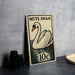 A vintage postage stamp featuring a swan illustration, placed on a dark surface next to some black camera lenses.
