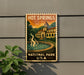 A vintage-style poster for Hot Springs National Park, featuring a building and a fountain, is displayed on a wall next to a plant.