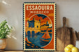 A vintage-style metal sign with a colorful illustration of a castle, boats, and a river, along with the text "ESSAOUIRA MOROCCO" on it, is displayed on a shelf next to a wooden cutting board and some potted plants.