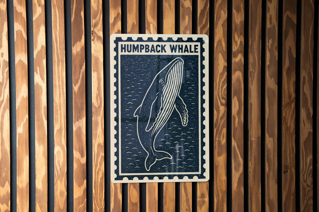 a blue and white sign with a picture of a humpback whale, mounted on a wooden wall.