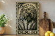 a large black and white stamp-like artwork depicting a shaggy dog's face, with the word "KOMONDO" written below it. The artwork is displayed on a shelf next to a wooden cutting board, a potted plant, and some lemons.