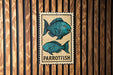 a sign with a parrotfish illustration on it, mounted on a wooden wall.
