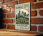 A metal sign with the text "KANSAS CITY MISSOURI USA" and an illustration of a city skyline, mounted on a brick wall.