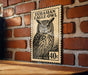 a large, detailed stamp-like artwork of an owl, mounted on a brick wall.